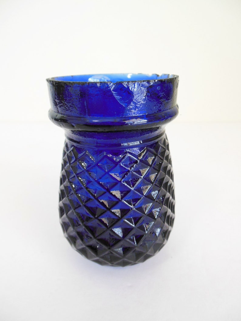 May include: A cobalt blue glass vase with a diamond pattern. The vase has a slightly chipped rim.