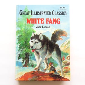 May include: A hardcover book titled "White Fang" by Jack London. The cover features a large, illustrated husky dog with a snowy mountain backdrop. The book is part of the "Great Illustrated Classics" series.