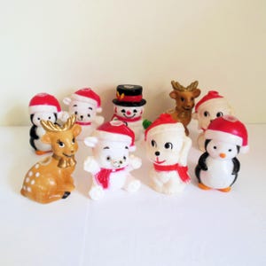 May include: A collection of ten vintage Christmas candle holders featuring a variety of animals and a snowman. The candle holders are made of white plastic and have red Santa hats. The animals include a penguin, a reindeer, a polar bear, and a lamb.