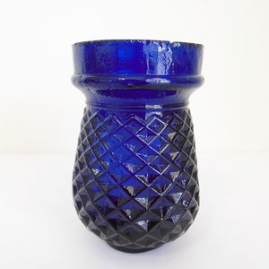 May include: A cobalt blue glass vase with a diamond pattern. The vase has a wide mouth and a rounded base.