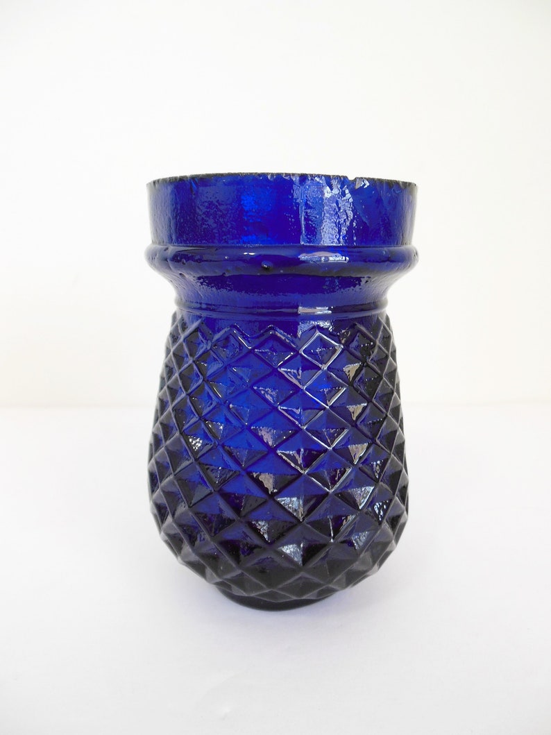 May include: A cobalt blue glass vase with a diamond pattern. The vase has a wide mouth and a rounded base.