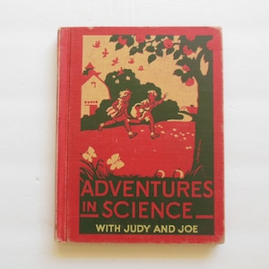 May include: A red book with a green and yellow illustration of two children walking in a field. The book title is "Adventures in Science" with the subtitle "With Judy and Joe".
