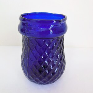 May include: A cobalt blue glass vase with a diamond pattern. The vase has a wide mouth and a rounded bottom.