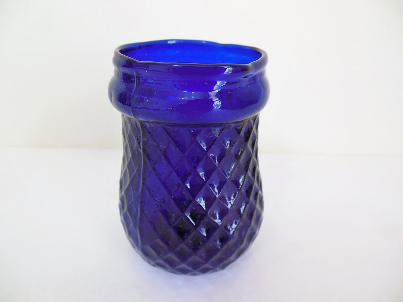 May include: A cobalt blue glass vase with a diamond pattern. The vase has a wide mouth and a rounded bottom.
