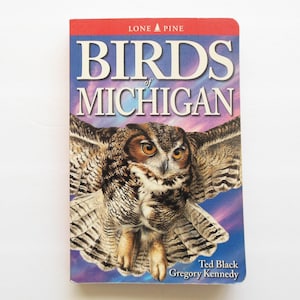 May include: A book titled "Birds of Michigan" with a vibrant cover featuring a detailed illustration of an owl with outstretched wings. The book has a red top banner and the authors' names are at the bottom.