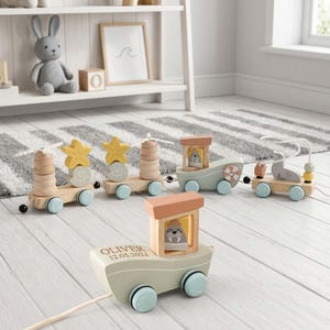 Puede incluir: Un tren de juguete de madera para arrastrar con vagones de colores pastel y formas marinas como estrellas de mar, conchas y una morsa. La locomotora delantera está personalizada con el nombre OLIVER y la fecha 12.05.2024 en letras negras.