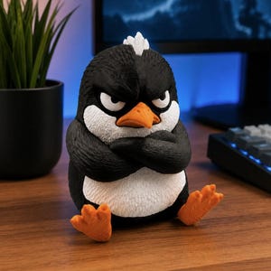 Könnte beinhalten: Eine kleine, texturierte Pinguin-Figur mit schwarz-weißem Gefieder, einem orangefarbenen Schnabel und orangefarbenen Füßen. Der Pinguin hat einen mürrischen Gesichtsausdruck mit gerunzelten Brauen und verschränkten Flügeln in sitzender Haltung.