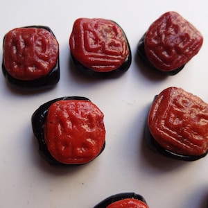 May include: Six red and black square-shaped beads with a raised design. The beads are made of a smooth, glossy material.