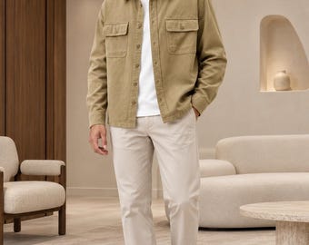 May include: A tan long-sleeved button-down shirt with two chest pockets worn over a plain white t-shirt, paired with light beige trousers and white sneakers. The outfit features a neutral color palette and a structured, layered design.