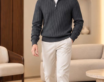 May include: A dark charcoal gray ribbed knit sweater featuring a quarter-zip collar, worn over a white t-shirt, paired with light beige trousers and clean white sneakers. The sweater has long sleeves with ribbed cuffs and a matching ribbed hem.