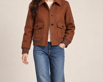 May include: A brown collared jacket with a button-front closure, two front flap pockets, and ribbed cuffs, worn over a white top with blue denim jeans and brown shoes. The jacket features a structured fit with long sleeves and a solid color.