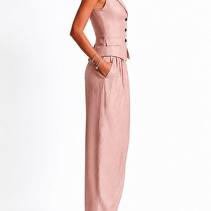 May include: A sleeveless dusty pink vest with a notched lapel and three dark buttons, paired with matching high-waisted wide-leg trousers featuring side pockets. The ensemble is crafted from a textured fabric and presents a tailored silhouette.