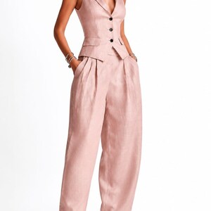 May include: A dusty rose sleeveless vest and matching wide-leg trousers set. The vest features a notched lapel, a deep V-neckline, and three dark buttons down the front. The trousers have a high-waisted fit with pleats and side pockets.
