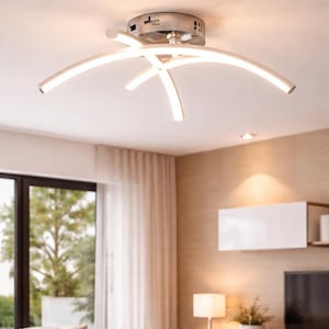 Könnte beinhalten: Moderne, weiße LED-Deckenleuchte mit gebürstetem Metallsockel. Das Licht hat ein geschwungenes, sich kreuzendes Design und sorgt für Umgebungsbeleuchtung. Die Leuchte ist an einer weißen Decke in einem Wohnzimmer angebracht.