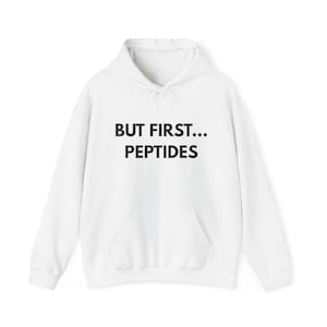 Puede incluir: Sudadera con capucha blanca con bolsillo delantero y cordón. El texto "BUT FIRST... PEPTIDES" está impreso en negro en el pecho. La sudadera es de estilo casual.