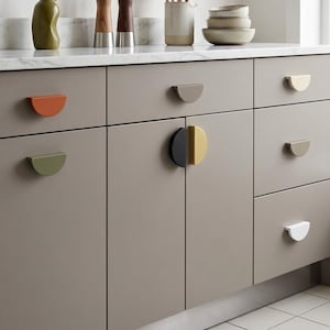 May include: A kitchen cabinet with various colorful, semi-circular cabinet pulls. The pulls are in shades of orange, green, gray, black, yellow, and white. The cabinets are a neutral gray color, and the countertop is white with gray veining.