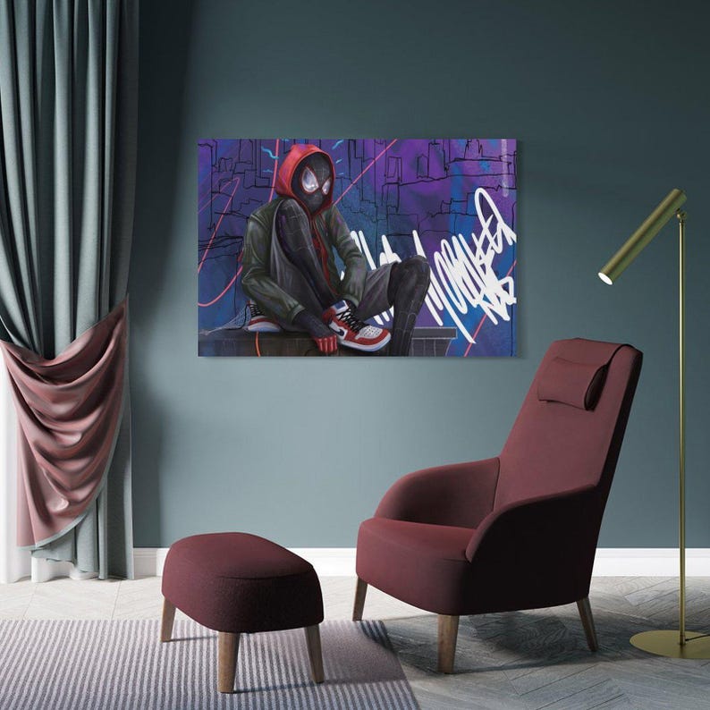 May include: A canvas print featuring a character in a red hooded jacket and black suit, with a mask, sitting against a graffiti-covered background. The artwork is displayed above a burgundy armchair and ottoman.