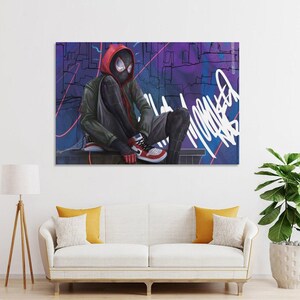May include: A framed art print featuring a character in a black and red suit with a red hood, seated against a purple and blue graffiti background. The character wears red, white, and black sneakers. The artwork is displayed above a white sofa.