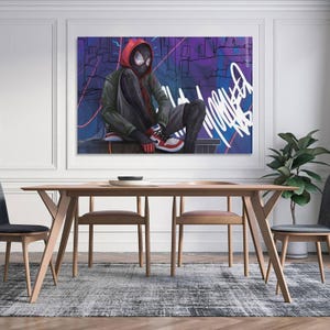 May include: A framed canvas art print featuring a seated superhero in a red and black suit with a red hood. The artwork has a graffiti-style background with purple and blue hues. The print is displayed above a wooden dining table.
