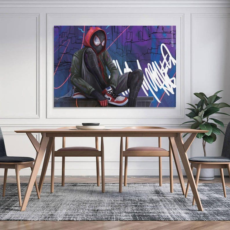 May include: A framed canvas art print featuring a seated superhero in a red and black suit with a red hood. The artwork has a graffiti-style background with purple and blue hues. The print is displayed above a wooden dining table.