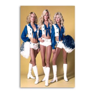 May include: Three women in vintage cheerleading outfits pose against a yellow background. They wear white shorts, white boots, and blue tops with star accents. Each holds a white and blue pom-pom.