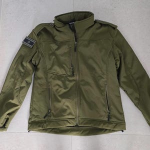 Puede incluir: Una taza de cerámica blanca con un asa negra y el texto "But First, Coffee" en negrita negra. La taza está sobre una superficie de madera. La taza mide aproximadamente 10 cm de alto.