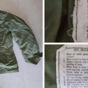 May include: An olive green military-style coat, viewed from above. The coat features a zipper, pockets, and a collar. The tag reads "COAT, COLD WEATHER, MAN'S, FIELD". The coat is a Large Regular size, with a chest size from 104 to 114 cm.