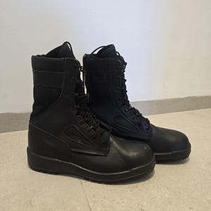 May include: A pair of black tactical boots featuring a high-top design with lace-up closures, reinforced toe caps, and a combination of smooth and textured panels. These boots have a sturdy construction with padded collars and thick rubber soles.