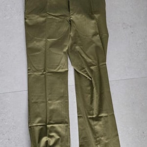 May include: Olive green trousers with a button and zip fastening. The trousers feature a classic five-pocket design and a slightly flared leg. The fabric has a subtle sheen, possibly a blend. Suitable for casual or semi-formal occasions. The length is approximately 100 cm.