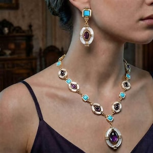 Può includere: Un set di gioielli color oro composto da una collana e un orecchino abbinato. I pezzi presentano cornici ovali bianche, pietre turchesi quadrate e gemme cabochon viola centrali. La collana è dotata di un grande ciondolo e catena.