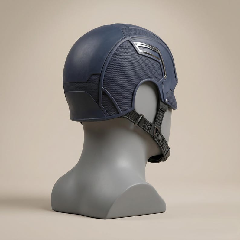 May include: A navy blue helmet with a textured design and silver accents, displayed on a gray mannequin head. The helmet features a chin strap and a detailed, geometric pattern. The overall design suggests a superhero or military theme.