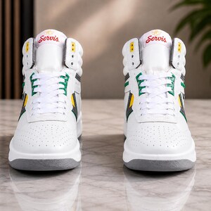 Puede incluir: Un par de zapatillas altas blancas con detalles en verde y amarillo. Las zapatillas tienen una suela gris y la palabra "Servis" en rojo en la leng&uuml;eta. El dise&ntilde;o incluye una puntera perforada y cierre con cordones.