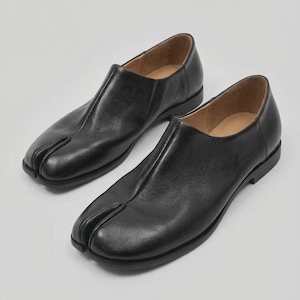 Op de afbeelding: Een paar zwarte leren schoenen met een split-teen. De schoenen hebben een uniek ontwerp met een apart gedeelte voor de grote teen. Ze hebben een lage hak en een gladde, gepolijste afwerking. De binnenkant is lichtbruin.