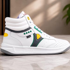 Puede incluir: Zapatilla alta blanca con detalles grises, amarillos y verdes. La zapatilla presenta la marca "Serra's" y un dise&ntilde;o perforado en la puntera. La suela es gris.