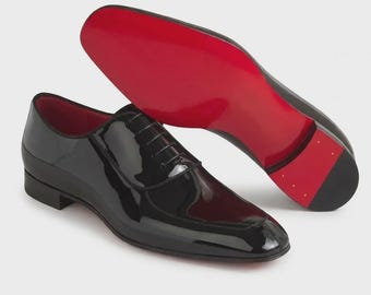 Puede incluir: Zapatos de vestir de charol negro con suelas rojas. Un zapato está de pie, el otro muestra la suela roja. Los zapatos tienen un diseño clásico con cordones y un acabado brillante. Diseño clásico.