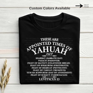 以下が含まれることがあります： 白文字の黒いTシャツ。「THESE ARE APPOINTED TIMES OF YAHUAH」というテキストと、その下に宗教的な祝日のリストがあります。シャツには「Leviticus 23」というテキストもあります。「Custom Colors Available」という言葉が一番上にあります。