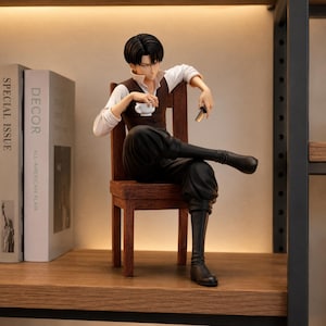 May include: A detailed anime-style figurine of a character with black hair, wearing a white shirt, brown vest, and black trousers, sitting on a wooden chair. The character holds a small white teacup in one hand and a small metallic object in the other.
