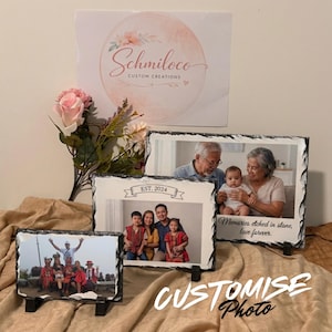 May include: Three rectangular slate photo plaques with rough, chiseled edges, each displaying a different family photograph. The plaques feature printed text including 'EST. 2024' and 'Memories etched in stone, love forever.' A pink artificial rose is placed behind the plaques.