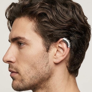 May include: A silver-toned ear cuff featuring a segmented, layered design that wraps around the upper cartilage of the ear. The metallic accessory has a smooth, polished finish and consists of multiple curved plates stacked together in a row.