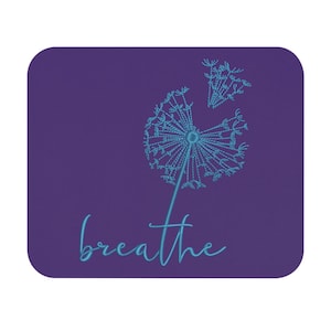 May include: A square, purple coaster features a teal dandelion design with the word "breathe" in a cursive font. The dandelion is partially blown, with some seeds floating away. The design is centered on the coaster.