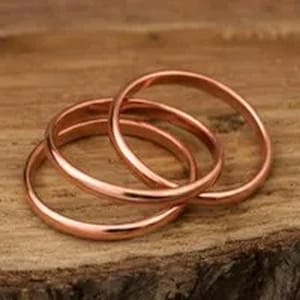 Op de afbeelding: Een set van drie in elkaar grijpende ringen gemaakt van gepolijst koper. Elke ring heeft een gladde, afgeronde band met een warme, metalen afwerking. De ringen zijn met elkaar verbonden en vormen een continue cirkelvormige structuur.