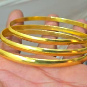 Peut inclure: Un ensemble de trois joncs fins et polis de couleur dorée avec une surface lisse et arrondie. Ces bracelets circulaires présentent une finition métallique réfléchissante et sont conçus pour être portés ensemble comme accessoire de poignet.