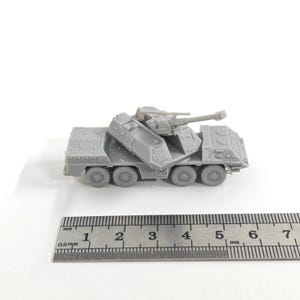 May include: A grey plastic model of a military vehicle, featuring multiple wheels and a large gun. The model has detailed compartments and features. A ruler is placed below the model for scale.