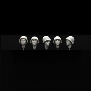 Może przedstawiać: Pięć szczegółowych miniaturowych rzeźb głów wojskowych, każda w białym hełmie. Szare głowy wyrażają różne emocje, zamontowane na cienkich, jasnych podporach na czarnym tle. Rzeźby wydają się być częścią zestawu modelarskiego.