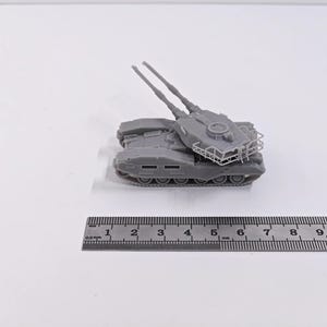 Peut inclure: Maquette de char grise avec deux canons surélevés et une tourelle détaillée. Le char repose sur un système de chenilles avec plusieurs roues. Une règle est placée en dessous, affichant des mesures en centimètres.