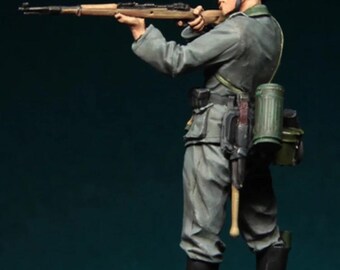 May include: A miniature figurine of a soldier in a gray uniform, helmet, and boots, aiming a rifle. The figure has a green gas mask canister and other gear attached to the uniform. The background is a dark teal color.