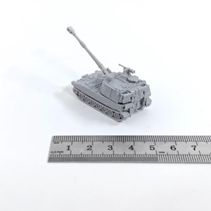 Puede incluir: Un modelo gris de tanque con un cañón largo y detalles precisos. El tanque está colocado sobre una superficie blanca junto a una regla. La regla mide en centímetros y milímetros.