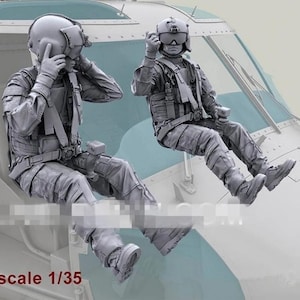 May include: Two gray scale model figures of helicopter pilots, seated in a cockpit. The figures are wearing helmets, flight suits, and tactical gear. The scale of the models is 1/35.
