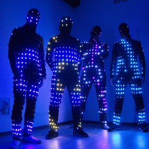 Può includere: Quattro tute integrali in tessuto nero ricoperte da serie di piccole luci LED luminose. Le luci emettono tonalità blu, bianche e magenta, creando un motivo a griglia sul busto, sulle braccia e sulle gambe di ogni tuta, inclusi i copricapi.