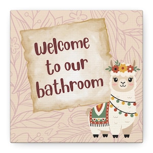 May include: Square bathroom sign with a light pink floral background. The sign features a llama wearing a flower crown and a decorative blanket. Text on the sign reads "Welcome to our bathroom."